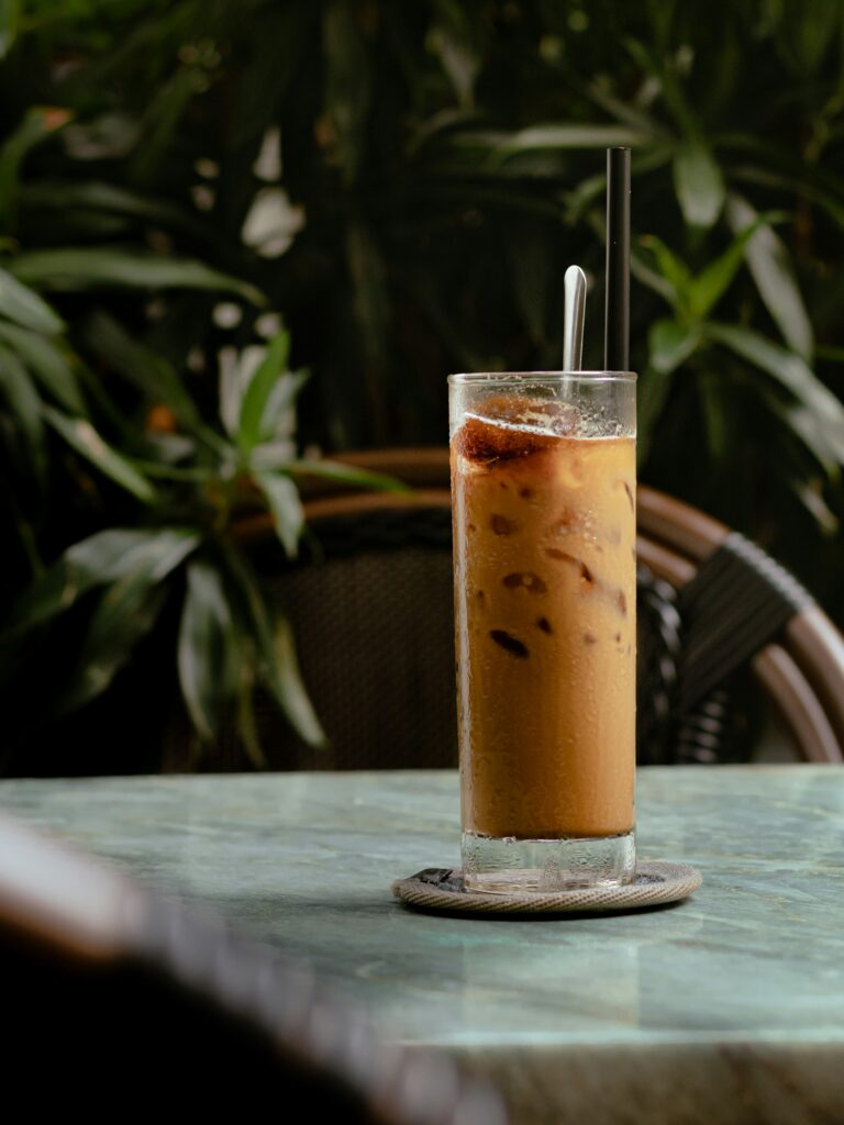 Ly cà phê đá Việt Nam trên bàn đá sáng màu, hậu cảnh quán cà phê xanh mát