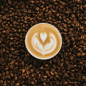Tách latte với hình trái tim trên lớp bọt sữa, bao quanh bởi hạt cà phê