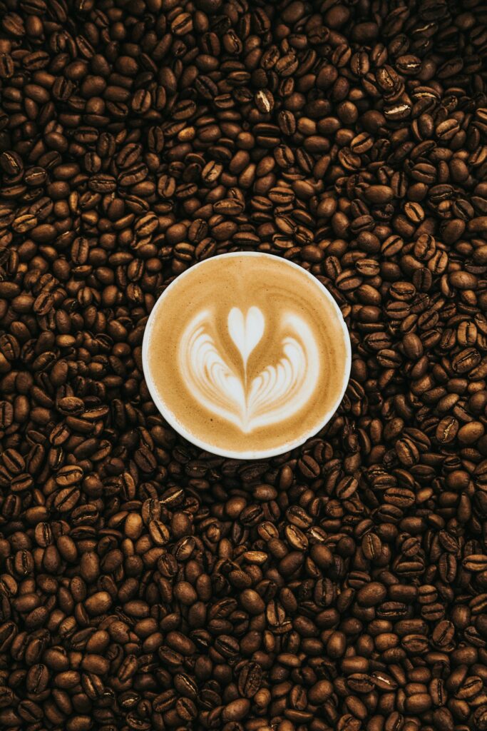 Tách latte với hình trái tim trên lớp bọt sữa, bao quanh bởi hạt cà phê