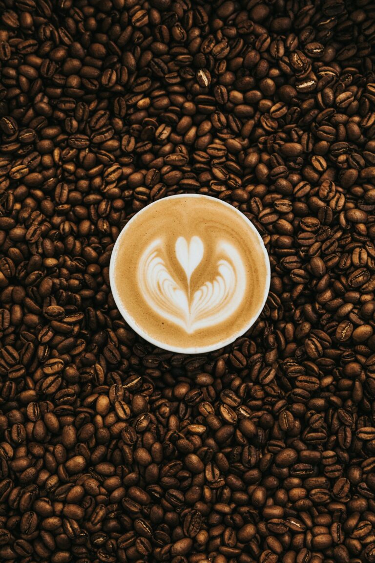 Tách latte với hình trái tim trên lớp bọt sữa, bao quanh bởi hạt cà phê